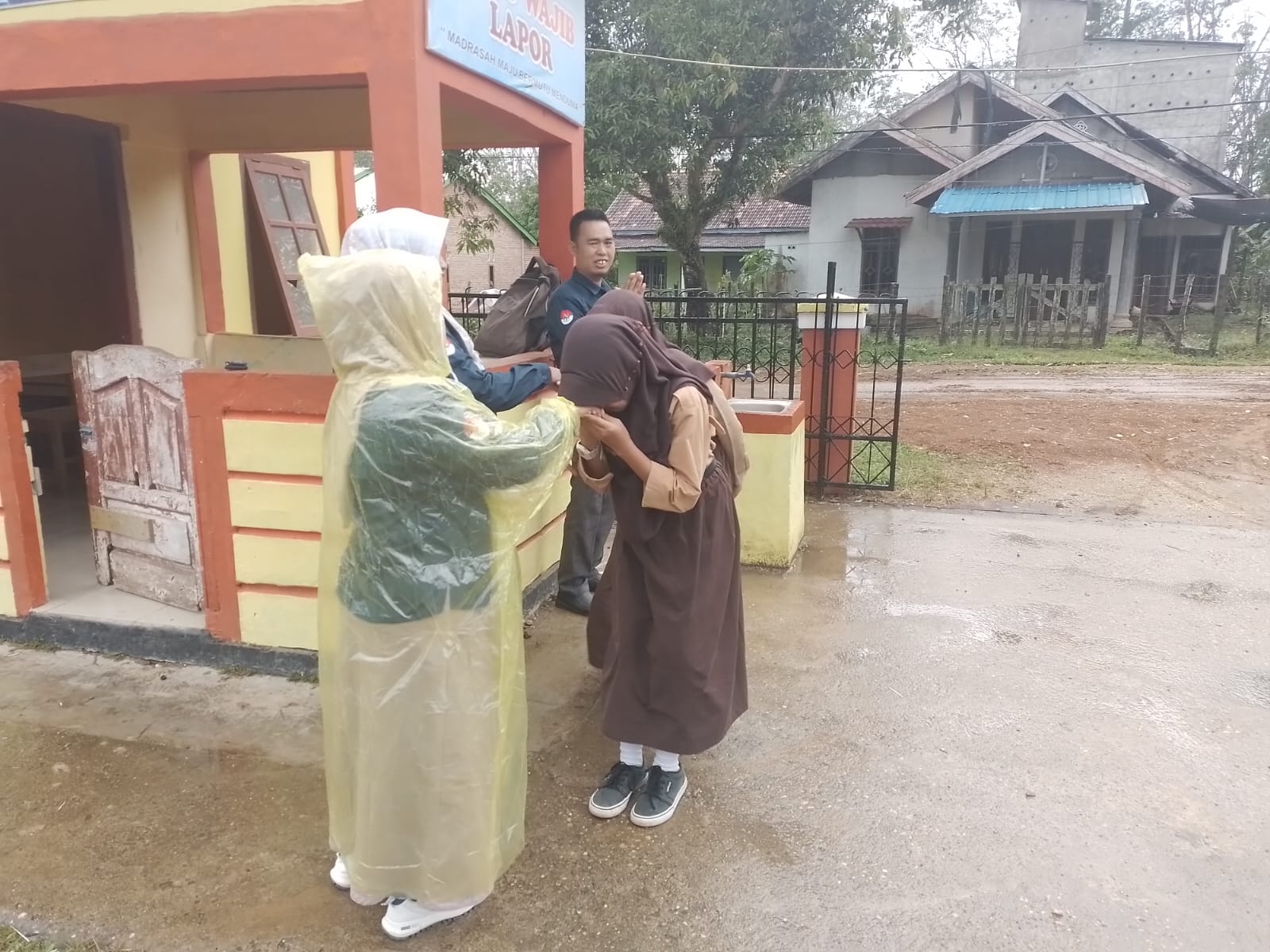 Meski Diguyur Hujan, Guru Piket Terakhir Tetap Tersenyum Menyambut Siswa